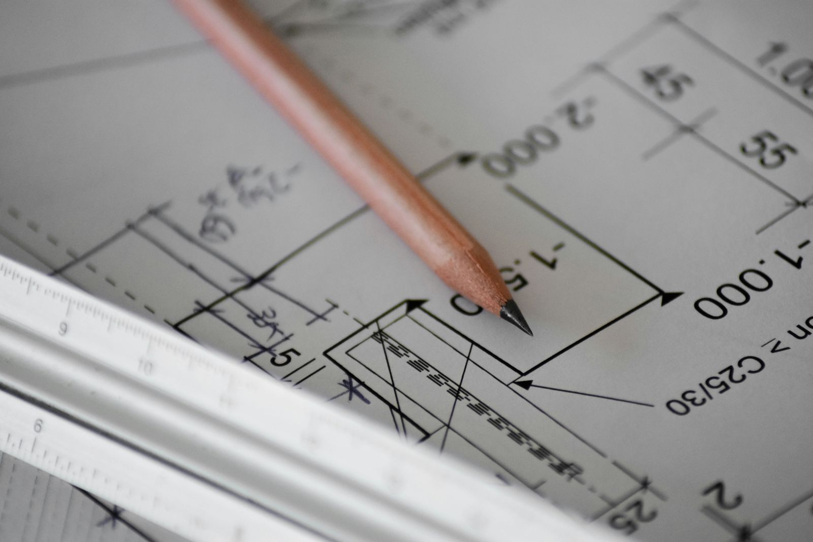 Un crayon posé sur un plan technique annoté de cotes, à côté d'une règle graduée.